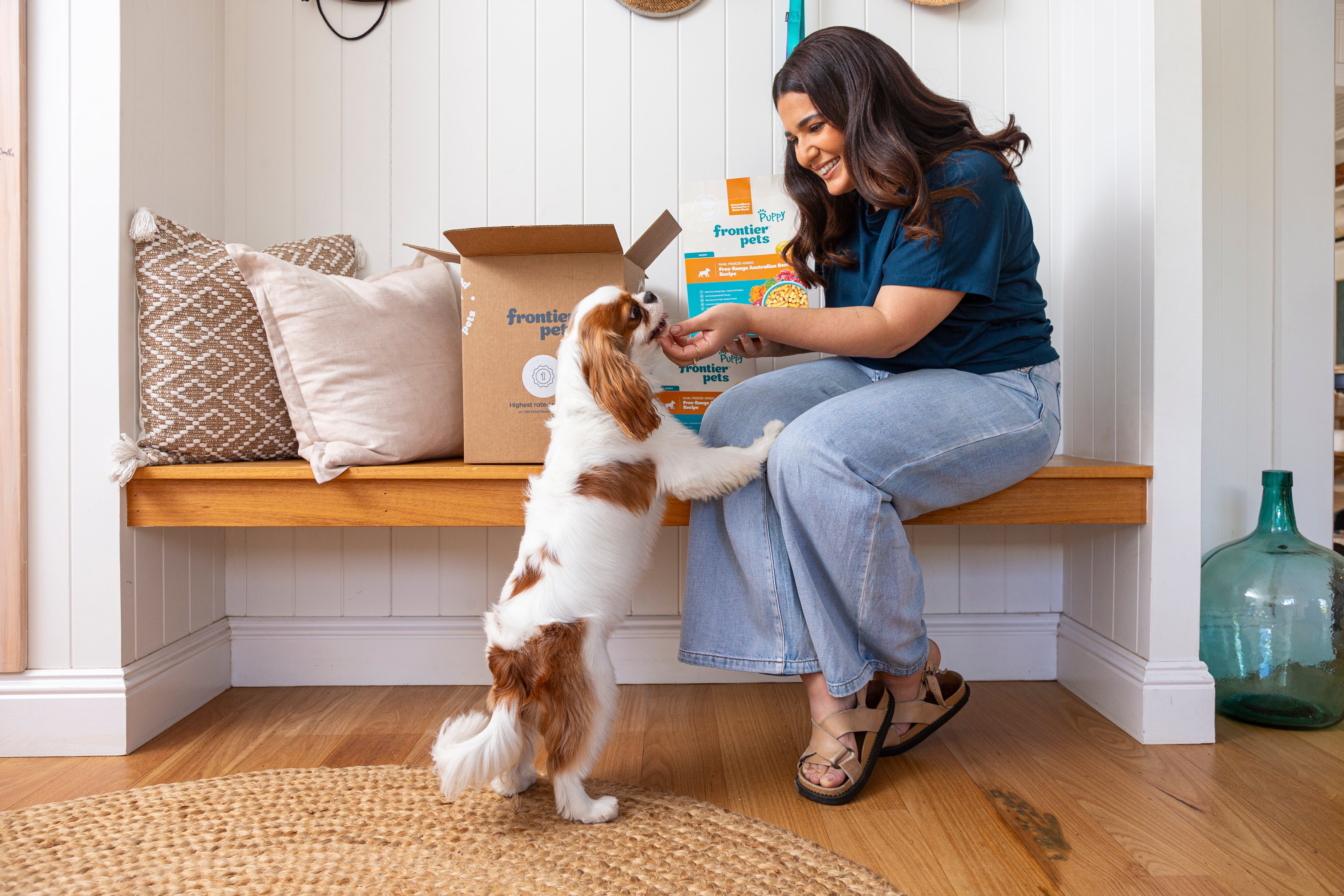 A Cavalier engaging playfully with women and exploring puppy food and a box.